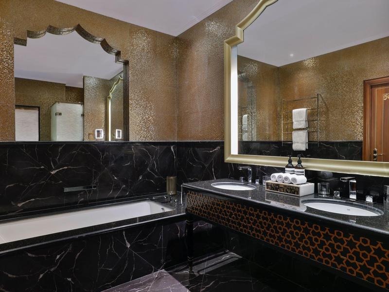 Luxuriöses Badezimmer mit Badewanne, großem Spiegel und dunkler Marmorverkleidung.