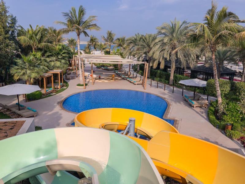 Blick auf einen Pool mit bunten Wasserrutschen und Palmen in einer tropischen Hotelanlage
