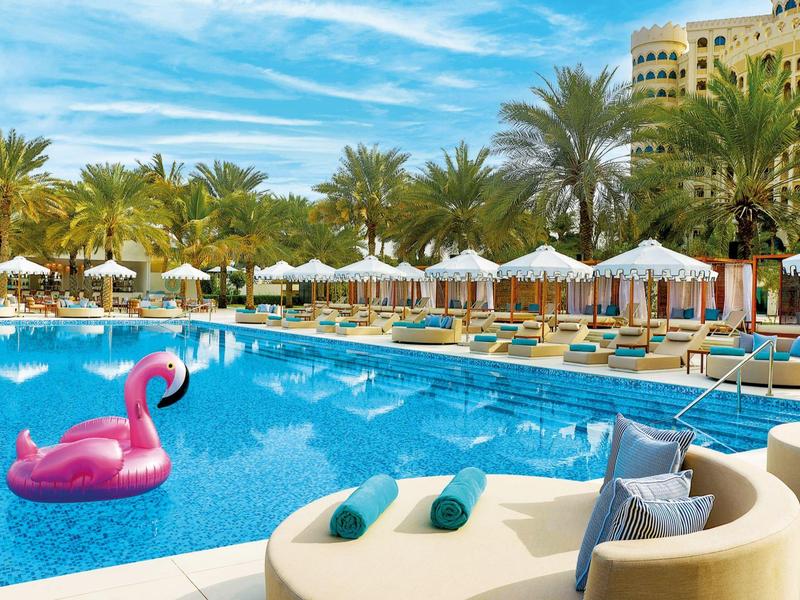 Großer Hotelpool mit Liegestühlen, Sonnenschirmen und einem pinken Flamingo-Schwimmring
