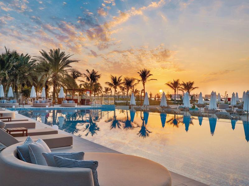 Sonnenuntergang über einem ruhigen Hotelpool mit Palmen und Liegestühlen.