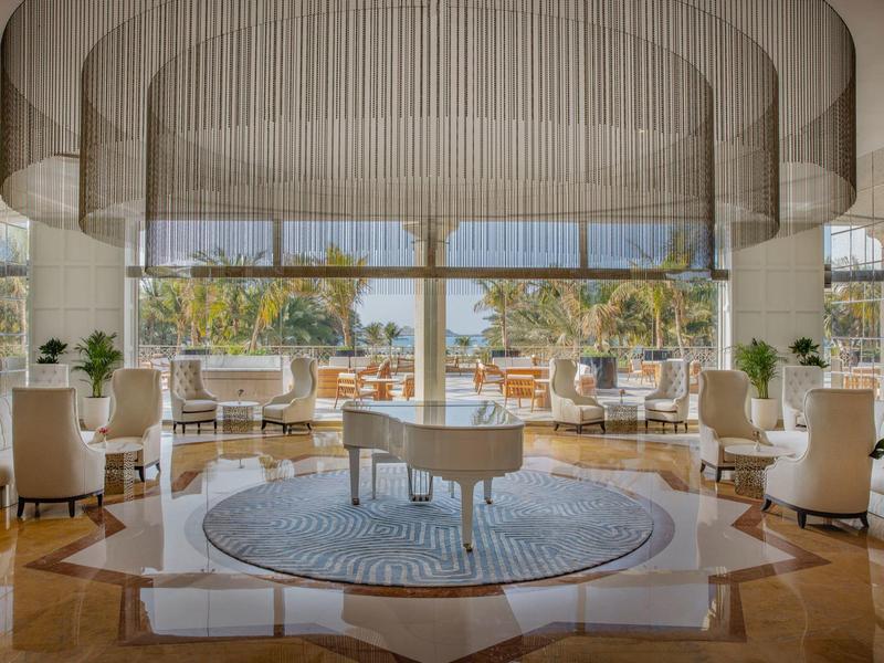 Elegante Hotellobby mit weißem Flügelklavier und großen Fenstern mit Blick auf eine sonnige Terrasse.