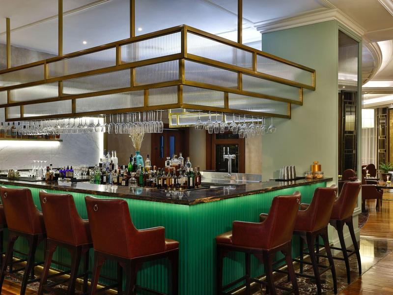 Moderner Hotelbarbereich mit grün beleuchtetem Tresen und roten Barhockern.