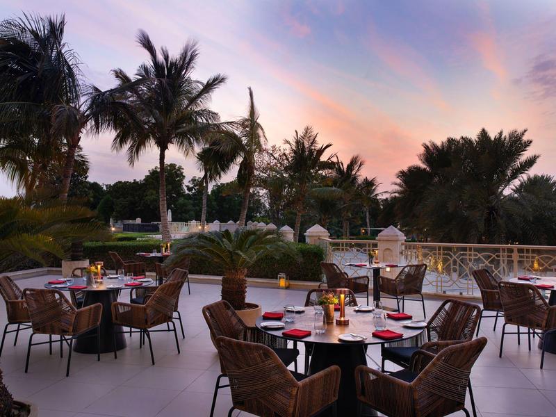 Terrasse mit gedeckten Tischen und Palmen bei Sonnenuntergang in einem Hotel