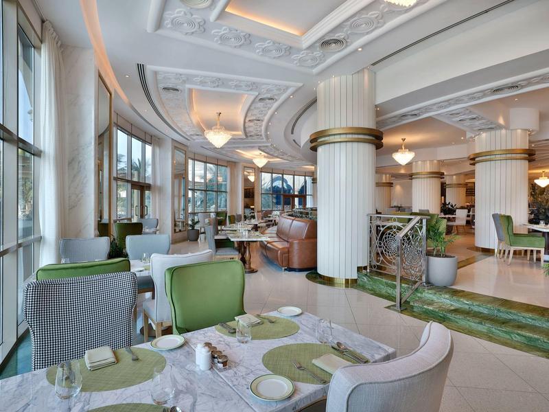 Elegantes Restaurantinterieur mit grünen und grauen Stühlen, großen Säulen und stilvollen Details.