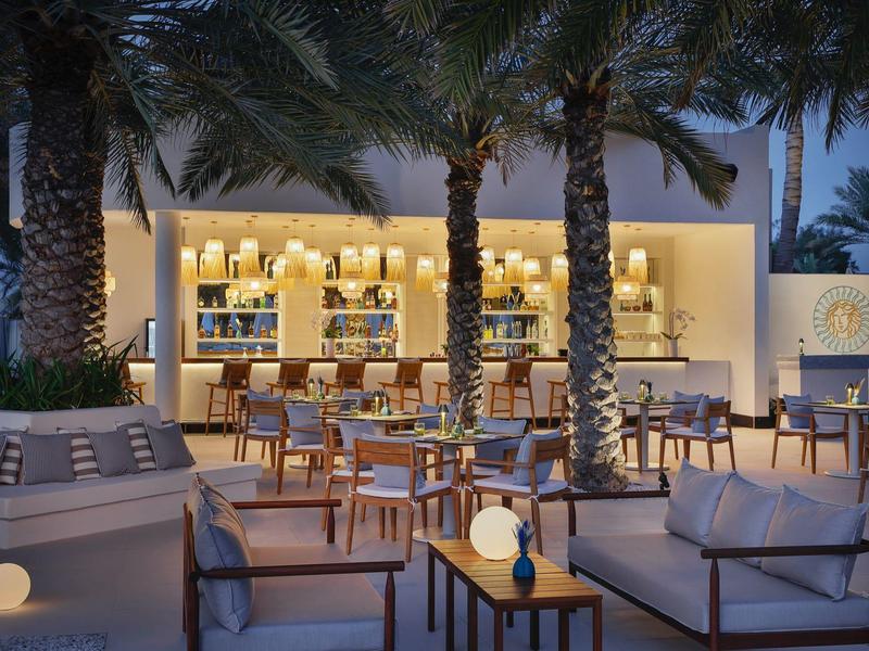 Abendliche Außenbar mit gemütlichen Sitzbereichen und Palmenbeleuchtung