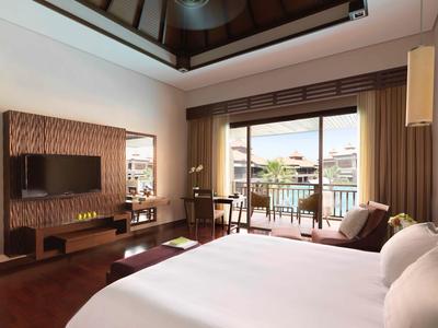 Modernes Hotelzimmer mit großem Bett, Fernseher, Balkon und Blick auf Wasser und Gebäude.