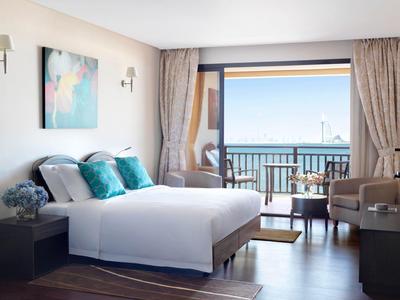 Helles Hotelzimmer mit großem Bett, Balkon und Blick aufs Meer bei klarem Himmel.