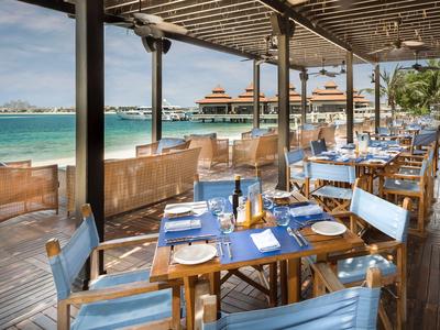 Restaurantterrasse mit blauen Stühlen und Blick auf das Meer und Hotelressort.