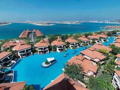 Blick auf Resort mit roten Dächern und großem Pool neben dem Meer.