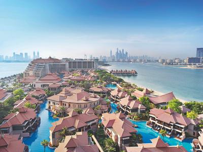 Luxuriöse Wasserbungalows und Hotelgebäude an der Küste mit klarem Himmel und Stadtblick.