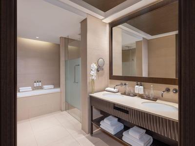 Salle de bain d'hôtel moderne avec baignoire, lavabo et grands miroirs dans des tons neutres.