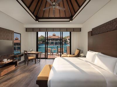 Chambre d'hôtel lumineuse avec grand lit, plafond en bois et vue sur piscine par grandes fenêtres.
