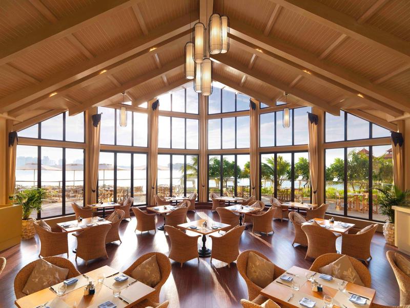 Großer, heller Speisesaal mit Holztischen und Stühlen, Panorama-Fenstern und Blick ins Freie.