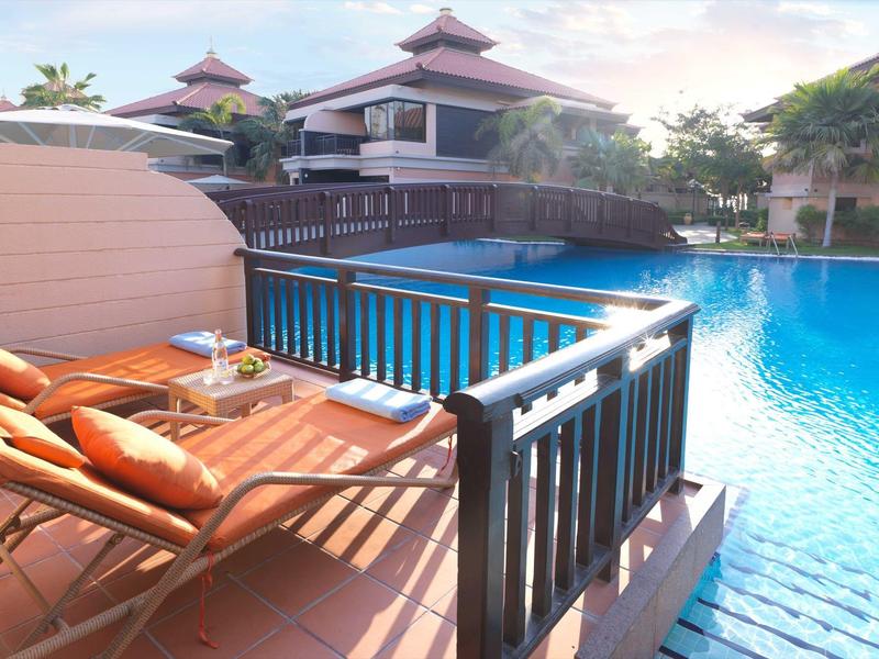 Sonnenterrasse mit zwei Liegestühlen neben klarem, blauem Pool und asiatisch inspirierten Gebäuden.