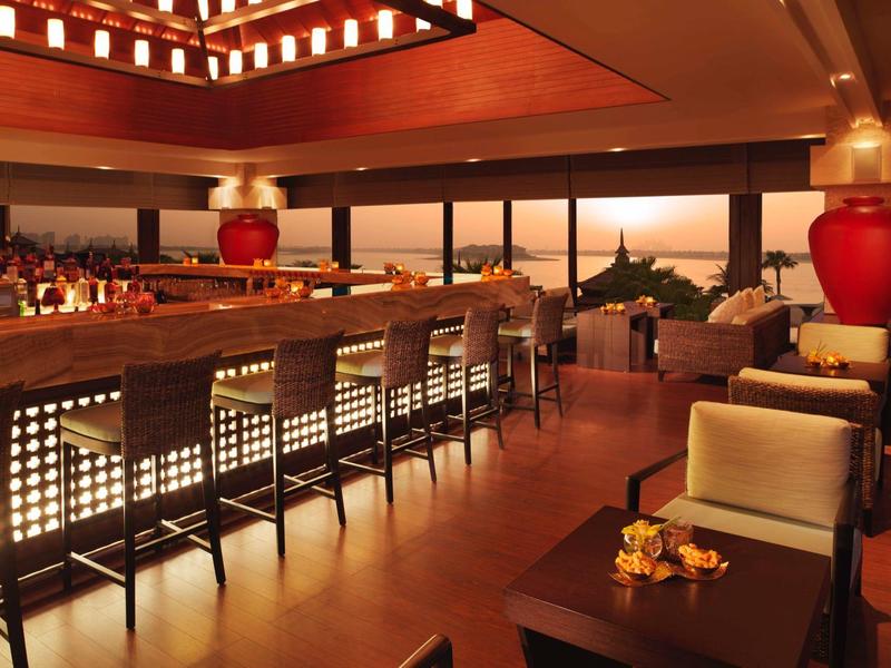 Moderne Bar mit langem, beleuchtetem Tresen, Holzboden, hohen Stühlen und gemütlichen Sitzbereichen.