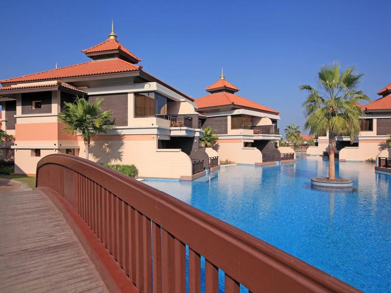 Luxuriöse Ferienvillen mit roten Dächern, Palmen und großem blauen Pool unter klarem Himmel.