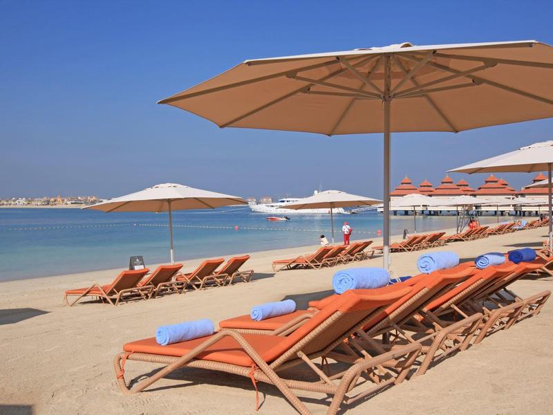 Sonnige Strandkulisse mit Reihen von Liegestühlen und großen Sonnenschirmen am klaren blauen Meer.