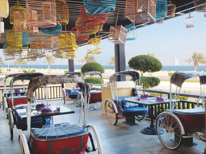Offene Terrasse mit Tischen und Vintage Fahrrad-Gestellen, Blick auf Meer und blauen Himmel.
