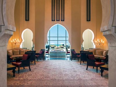 Luxuriöser Innenraum mit hohen Bögen, Sesseln, Teppichboden und Meerblick durch Fenster.