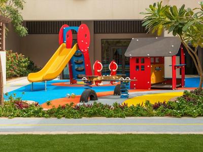 Kinderspielplatz mit Rutsche, Klettergerüst, Spielhaus und weichem blau-orangem Bodenbelag.