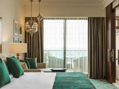 Elegantes Hotelzimmer in Grüntönen mit großem Bett, Sitzbereich und Blick auf Balkon.
