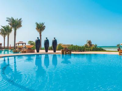 Lichte Poollandschaft mit Blick aufs offene Meer und Palmen unter klarem Himmel.