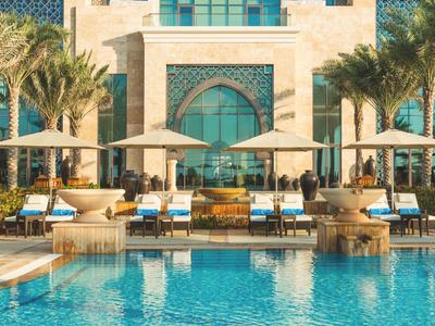 Luxuriöser Poolbereich mit Liegen und Sonnenschirmen vor einem hotelähnlichen Gebäude.