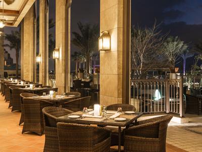 Abendliche Terrasse eines Hotels mit gedeckten Tischen und Korbsesseln bei warmem Licht.