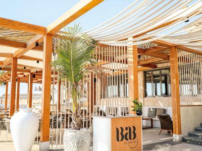 Moderner Eingangsbereich eines B&B mit Holzpergola, großen Pflanzgefäßen und Sitzbereich.