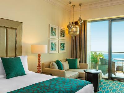 Helles Hotelzimmer mit Doppelbett, Sofa, bunten Kissen und Balkon mit Meerblick.