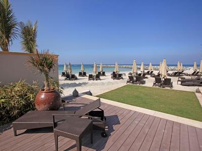 Terrasse mit Liegestühlen und Sonnenschirmen am Meer bei klarem Himmel.