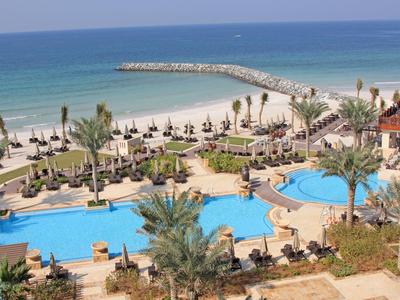 Blick auf Resort mit Pools, Palmen und Strand am ruhigen blauen Meer.
