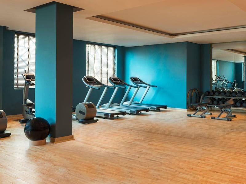 Moderner Fitnessraum mit Holzfußboden, hellblauen Wänden, Laufbändern und Hanteln.