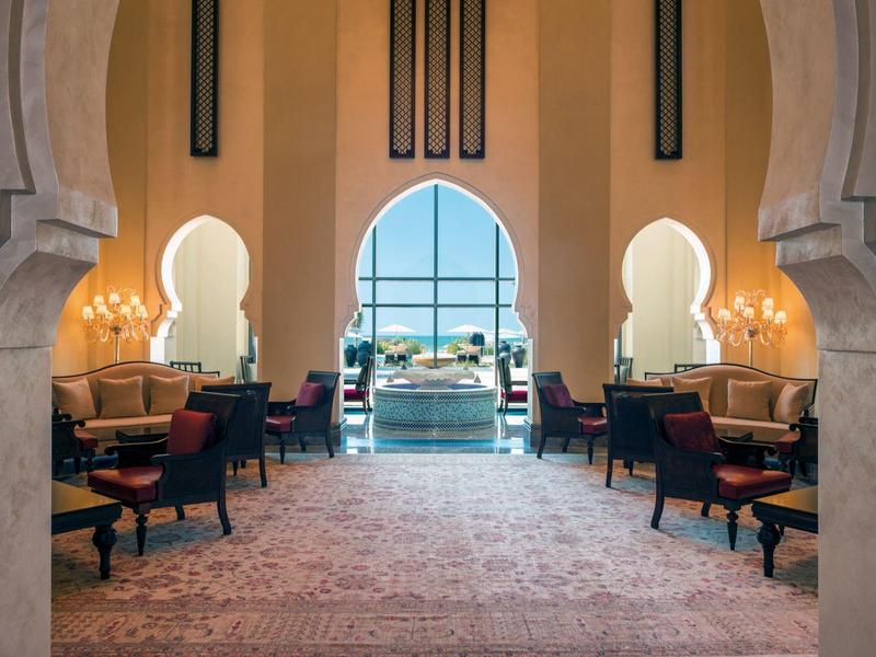 Luxuriöser Innenraum mit hohen Bögen, Sesseln, Teppichboden und Meerblick durch Fenster.