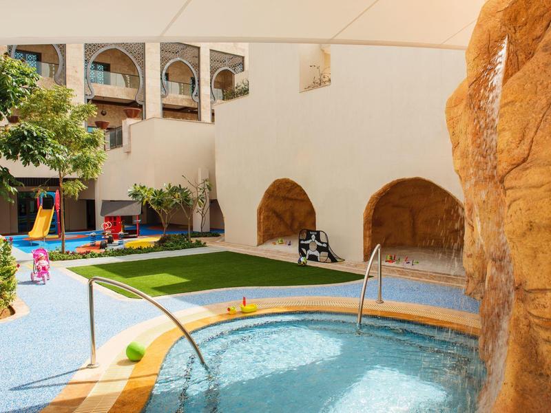 Innenhof mit kleinem Pool, grünem Rasen, Pflanzentopf und beigem Gebäude mit Bögen.