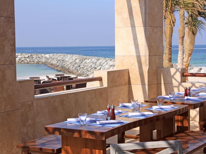 Gemütliche Terrasse mit dunklen Korbmöbeln und warmen Wandlampen bei Nacht.