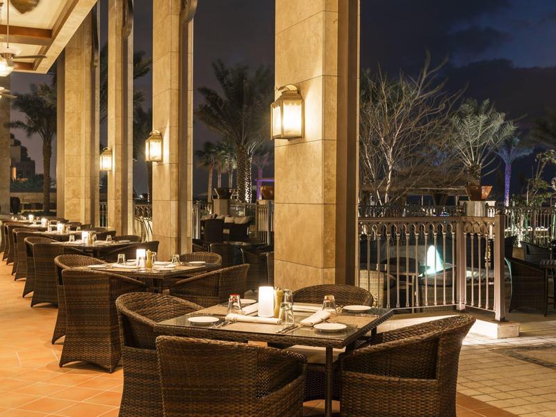 Gemütliche Terrasse mit dunklen Korbmöbeln und warmen Wandlampen bei Nacht.