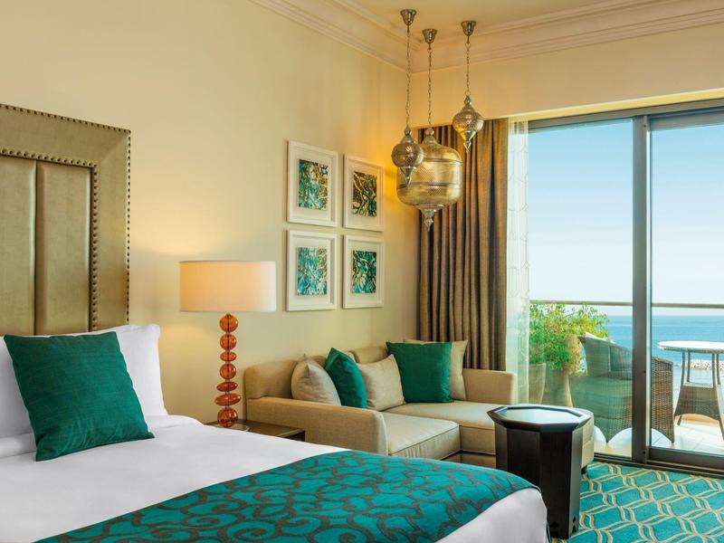 Helles Hotelzimmer mit Doppelbett, Sofa, bunten Kissen und Balkon mit Meerblick.