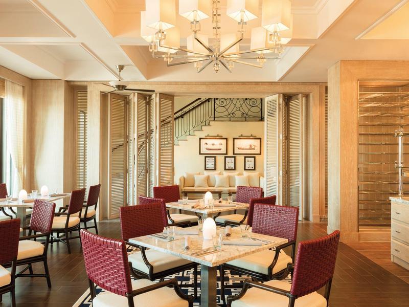 Moderner Gastraum mit Holz- und Glaselementen, roten Stühlen und einem Kronleuchter an der Decke.