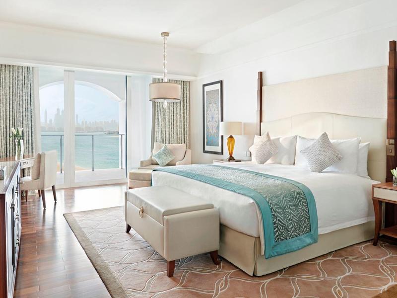 Helles Hotelzimmer mit großem Bett, türkisfarbenen Akzenten und Meerblick durch große Fenster.