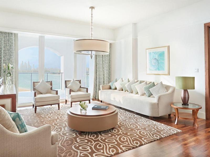 Helles Wohnzimmer mit weißen Möbeln, großem Teppich, Holzboden und Bergblick durch Fenster.