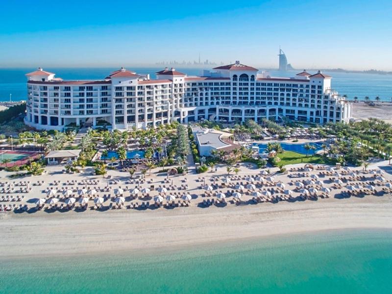 Großes Strandresort mit Hotel, Poolanlagen, Palmen und vielen Sonnenliegen am türkisfarbenen Meer.