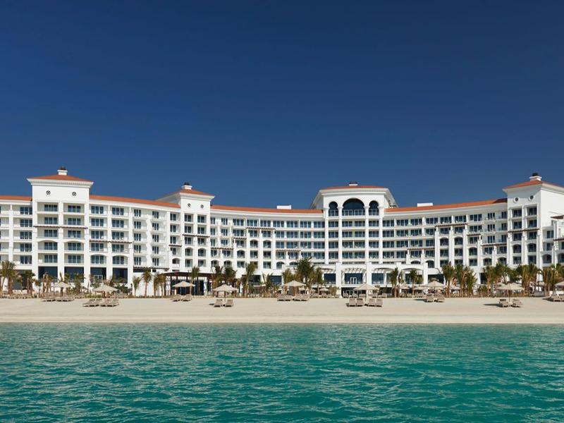 Großes weißes Hotel am Strand mit Palmen und klarem blauem Himmel im Hintergrund.