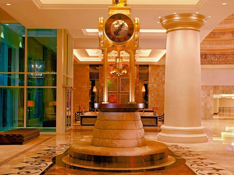 Große Standuhr mit goldenen Details steht auf Podest in elegantem, hell beleuchtetem Innenraum.