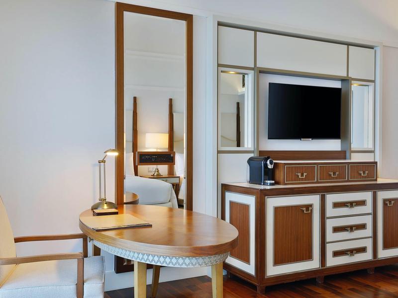 Modern eingerichtetes Zimmer mit runden Tisch, Spiegel, Stuhl und TV auf Kommode aus Holz.