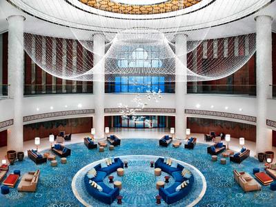 Großer Hotel-Lobby mit blauem Teppich, runden Sitzbereichen und prächtiger Deckenbeleuchtung.