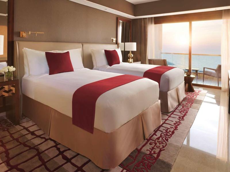 Luxuriöses Hotelzimmer mit zwei Doppelbetten, roten Akzenten und großer Glasfront mit Meerblick.