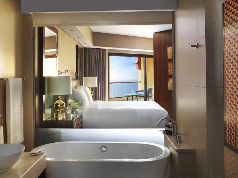 Modern eingerichtetes Badezimmer mit freistehender Badewanne und Blick auf ein Schlafzimmer und Meer.