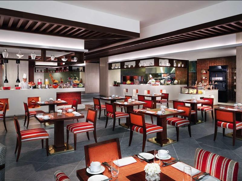 Modernes Restaurant mit roten Stühlen, dunklen Holztischen und offener Bar im Hintergrund.