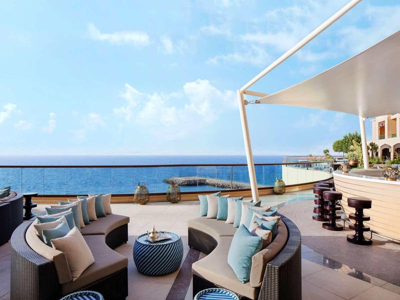 Moderner Außenbereich mit runden Sofas, blauen Kissen, Ozeanblick und weißem Sonnensegel.